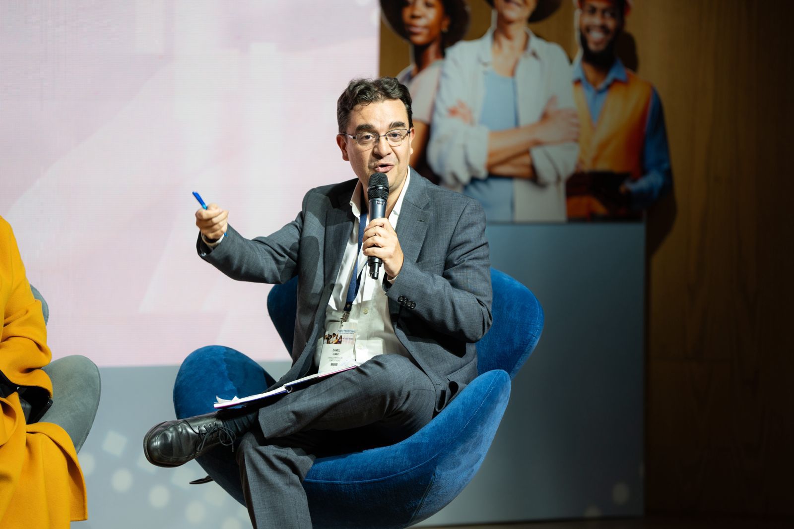 Persona hablando en un conversatorio con micrófono y apuntes en mano